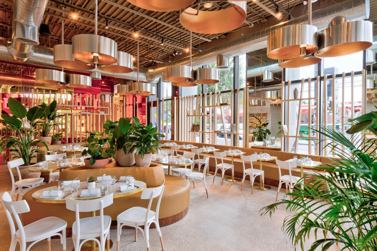 Modern restaurant interior with round tables, chairs, and decorative plants.